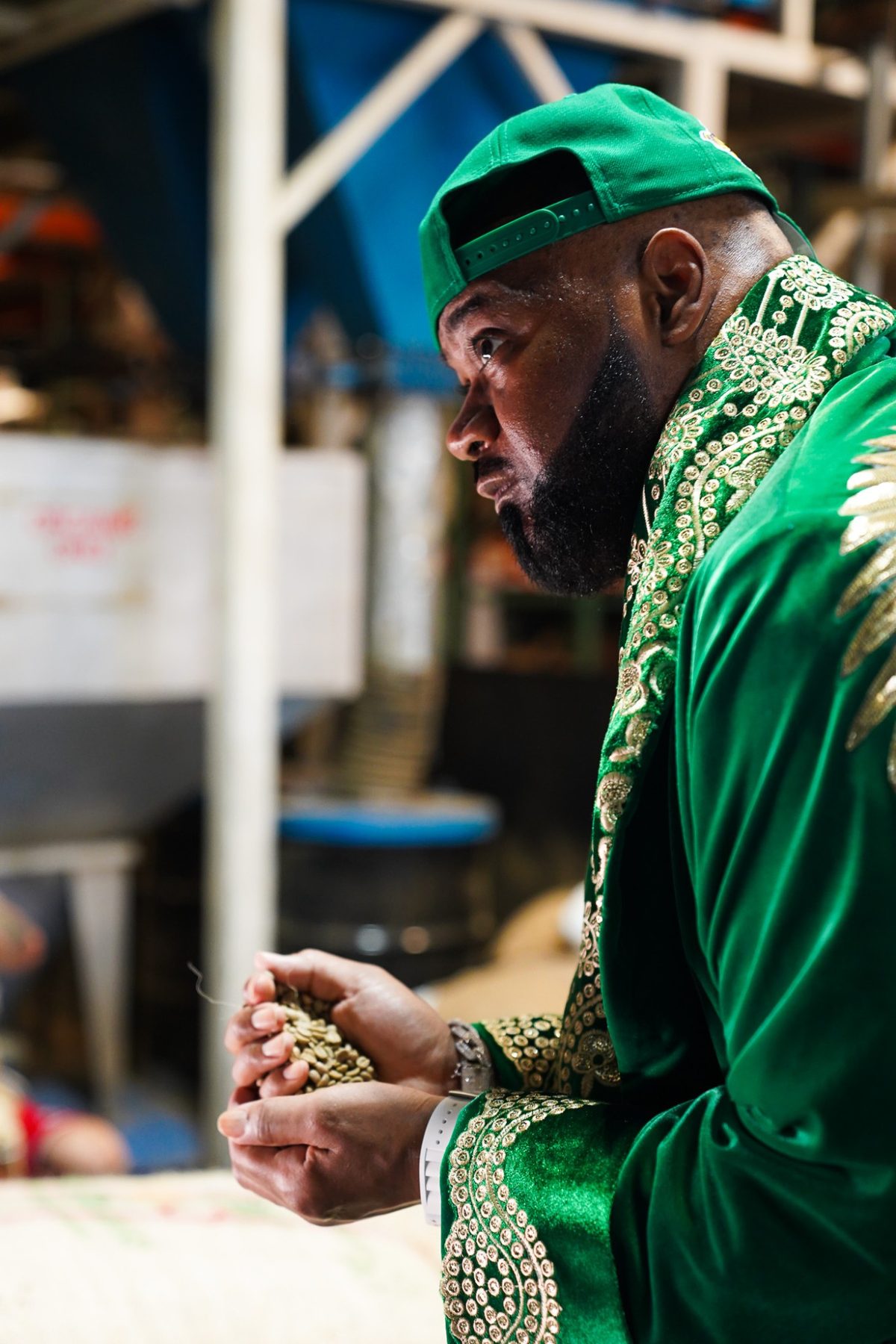 Ghostface Killah in profile in a green velvet robe, holding a handful of green coffee beans at the roastery for Killah Koffee