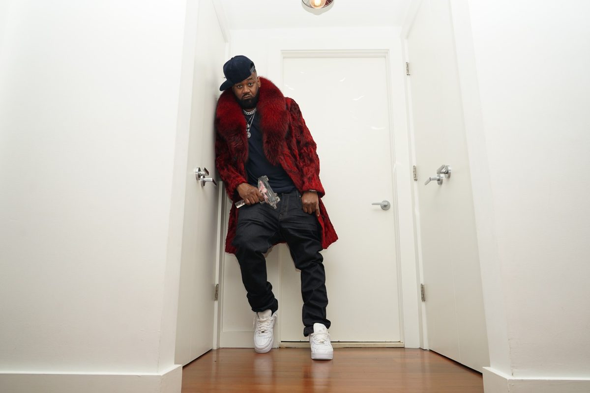 Ghostface Killah leaning in a white hallway in a red fur coat and white sneakers