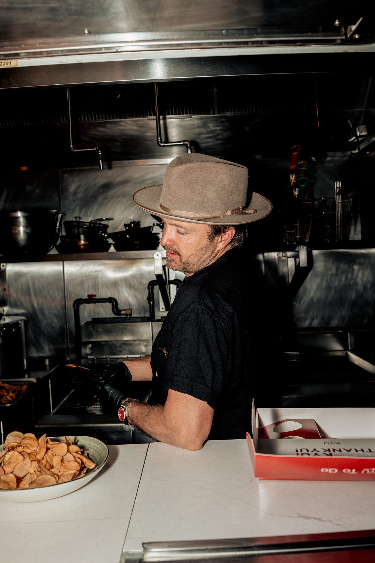 Aaron Paul working in the KYU kitchen beside a plate of chips and a red box