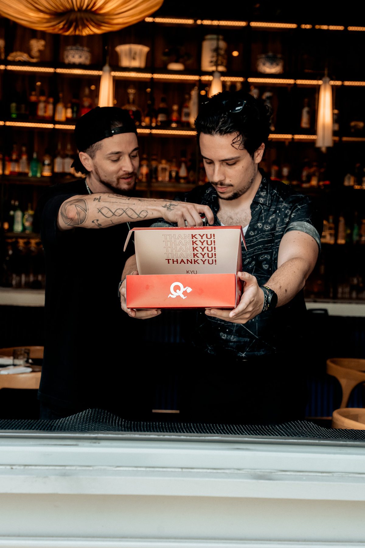 Two members of the KYU team opening a ThanKYU box at the bar