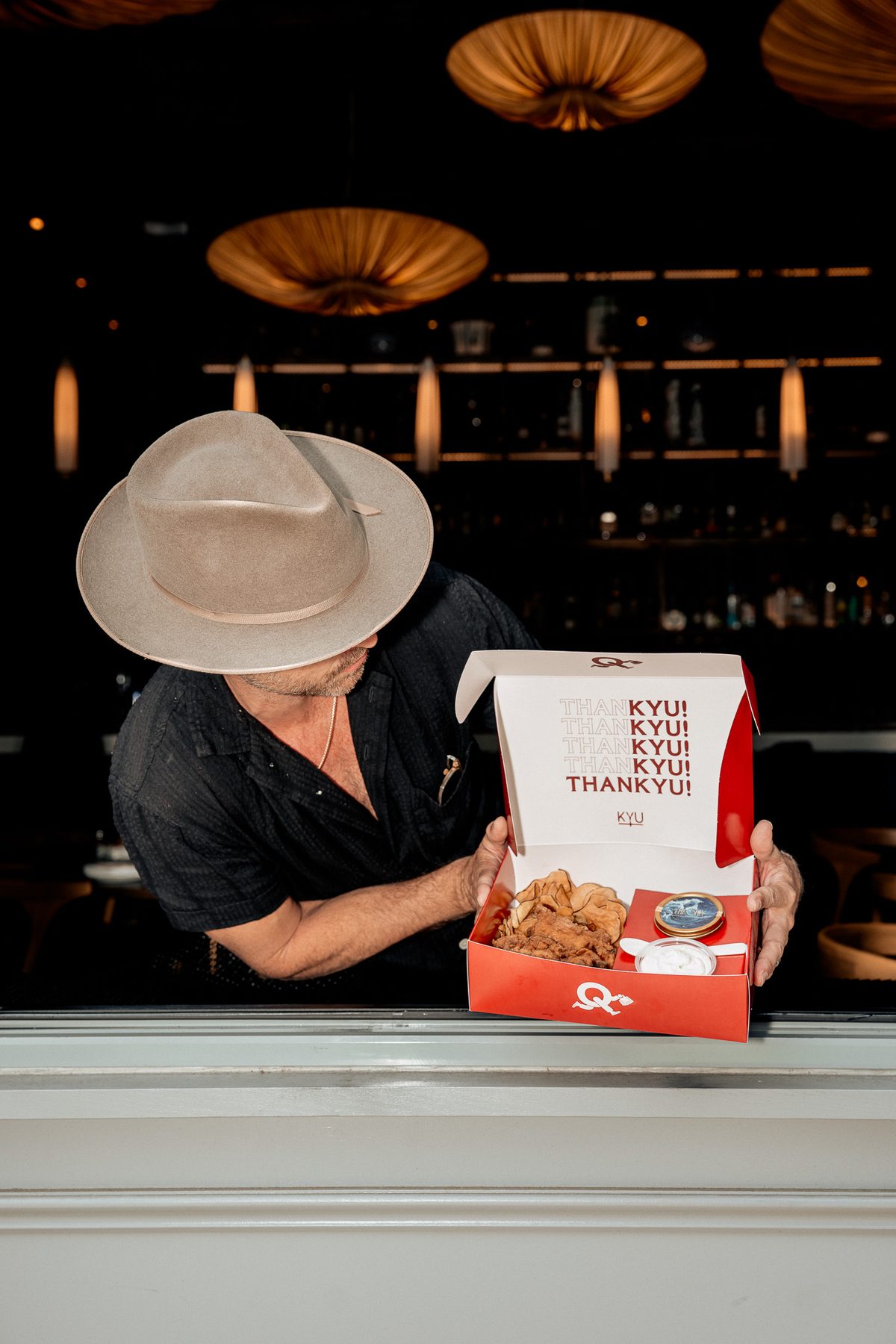 Aaron Paul, in his hat, leaning over an open box on the counter