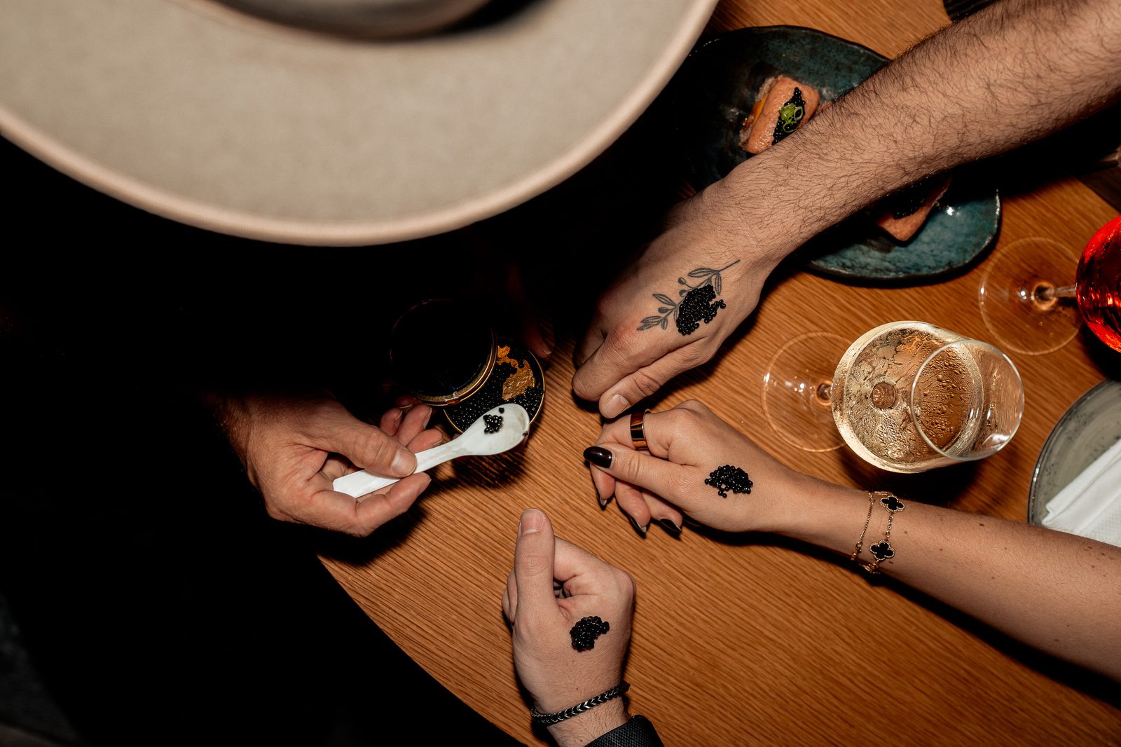 Overhead of caviar bumps on the back of hands around a wooden table