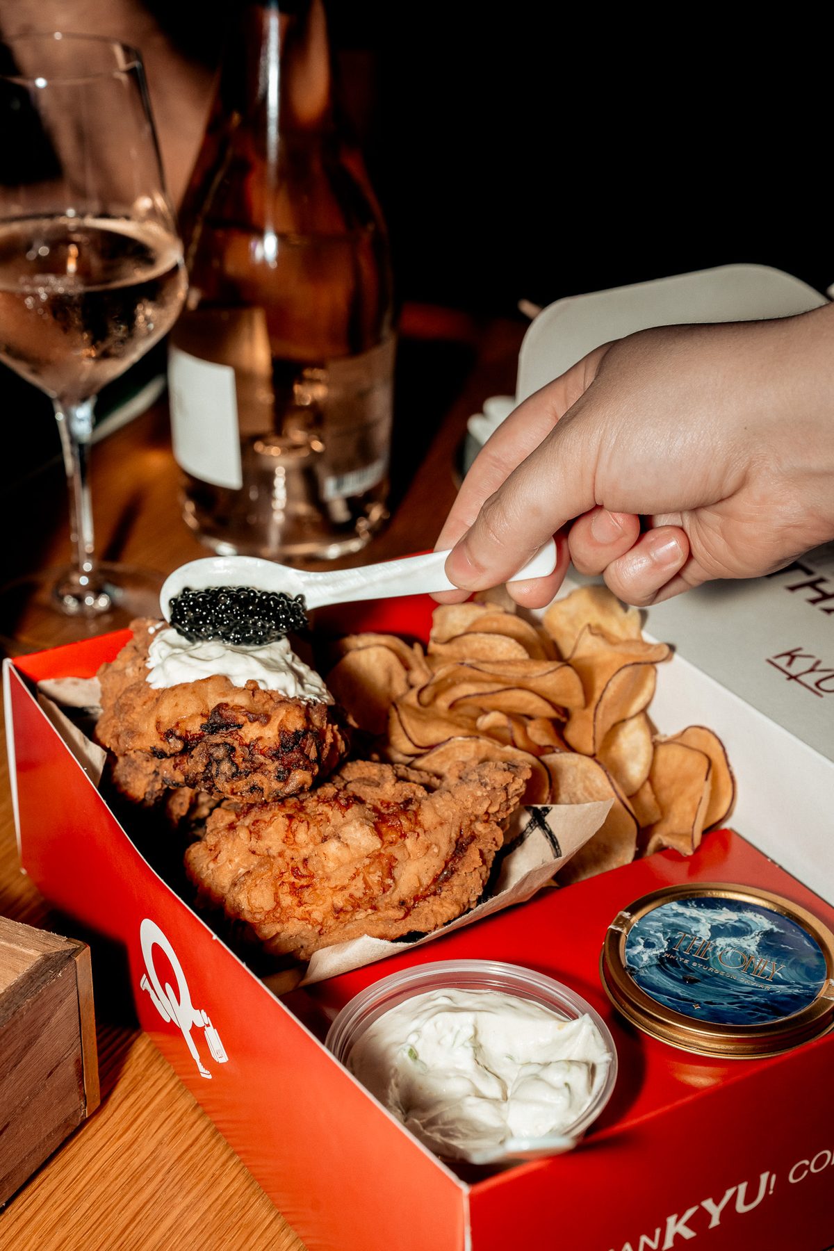 A spoon of caviar being added to fried chicken in the red box, with chips and dip