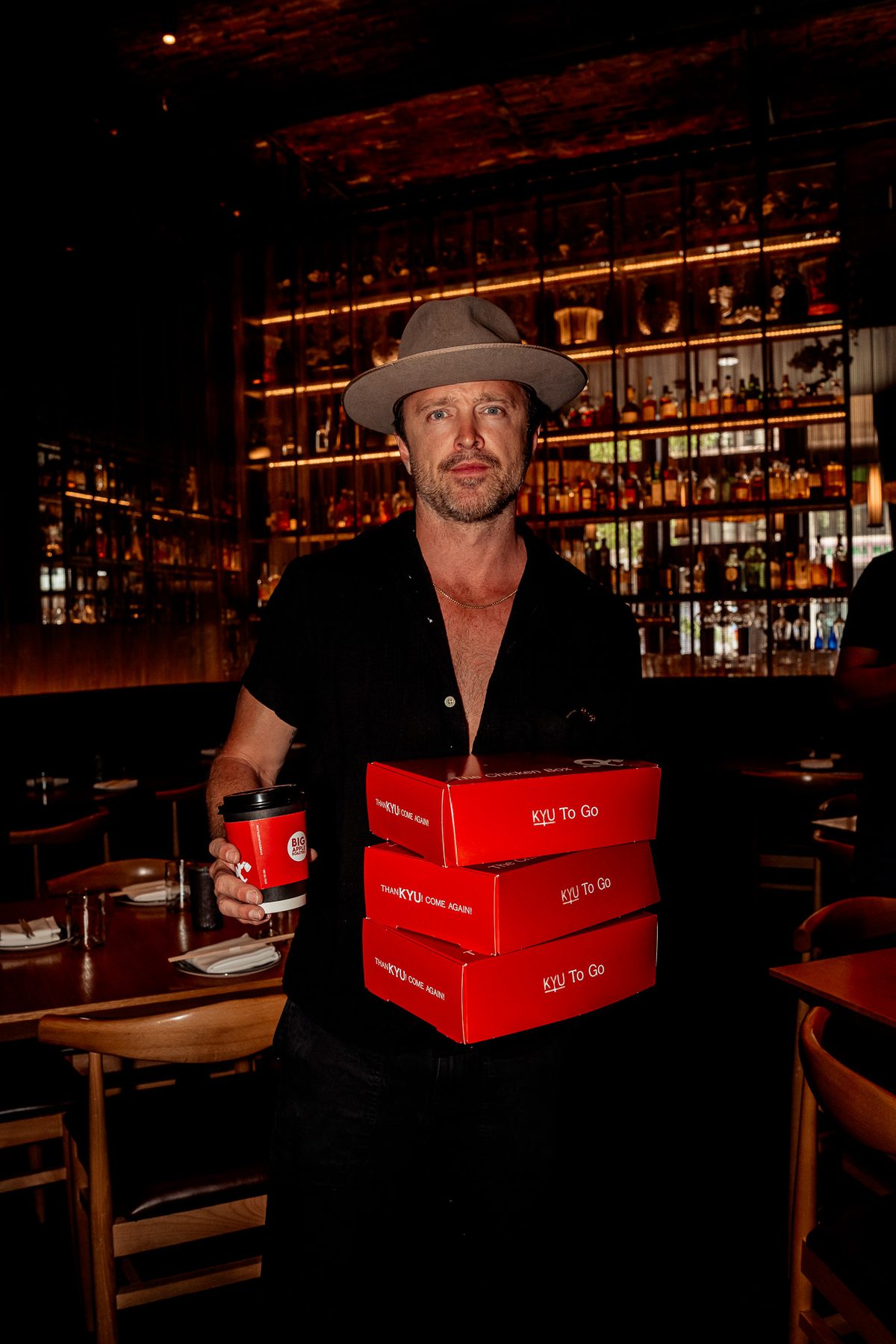 Aaron Paul at the bar with a stack of red boxes and a coffee cup
